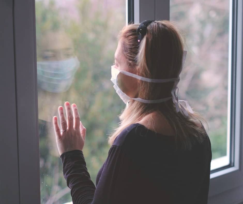 Woman alone with hospital mask staring out window