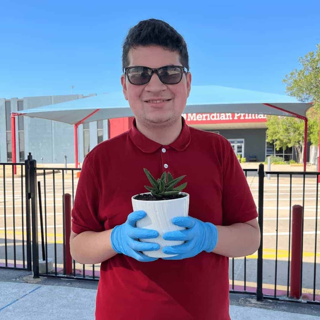 Daniel wearing sunglasses, smiling holding a plant in a pot.