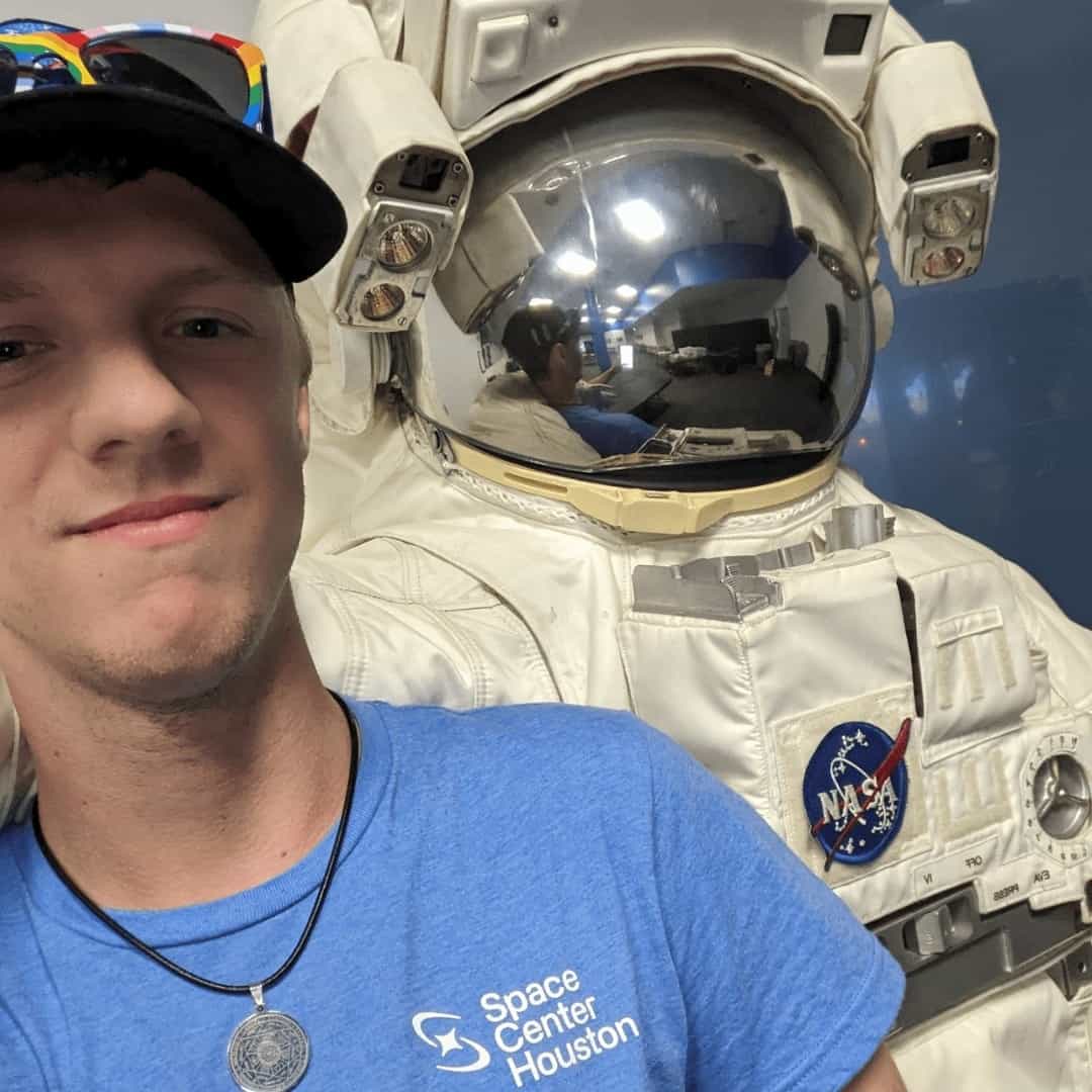 John posing with a space suite at Space Center Houston.
