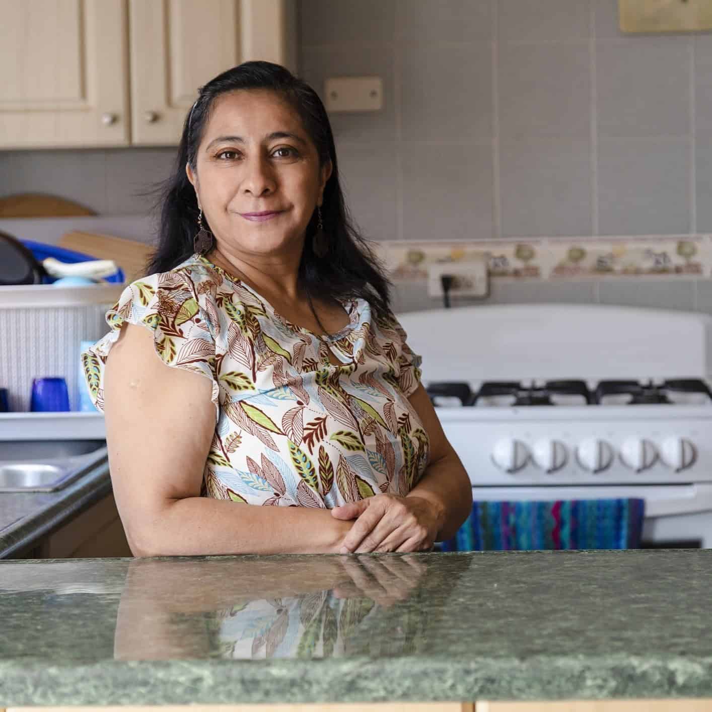 A Hispanic woman standing in her kitchen.