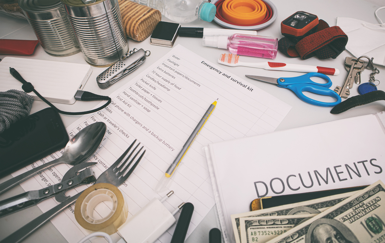Emergency items organized on a table. Documents, water, food, first aid kit and other items needed to survive.