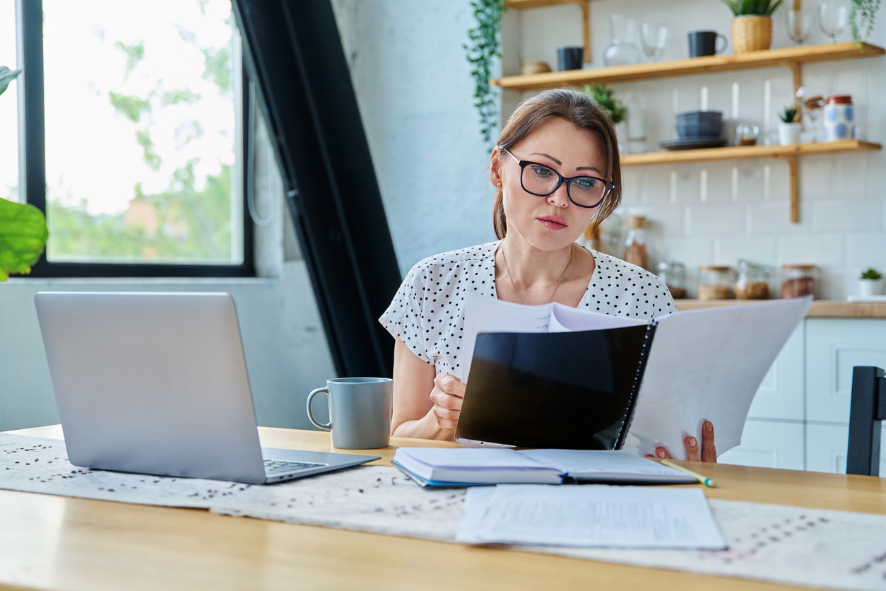 A woman sitting at a kitchen table reading and taking notes.