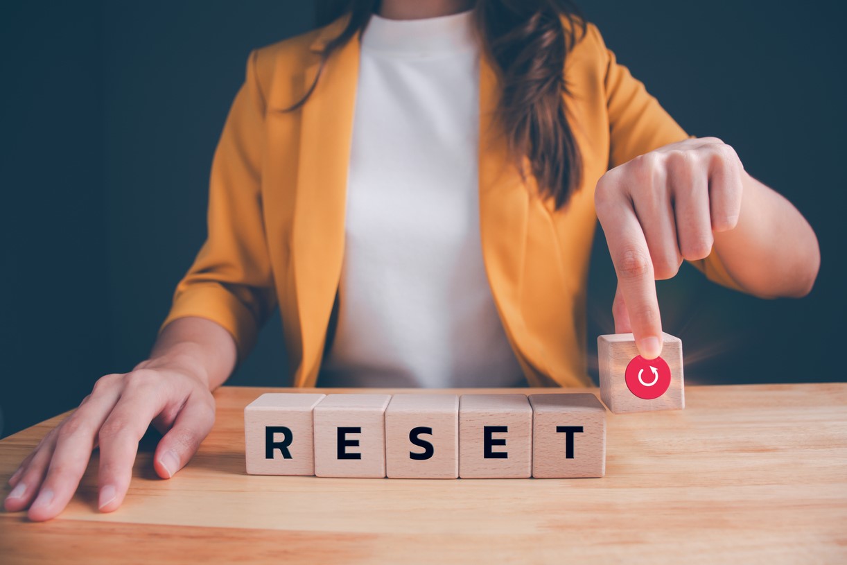 A woman sitting at a table with blocks that spell reset and one with a refresh icon it.