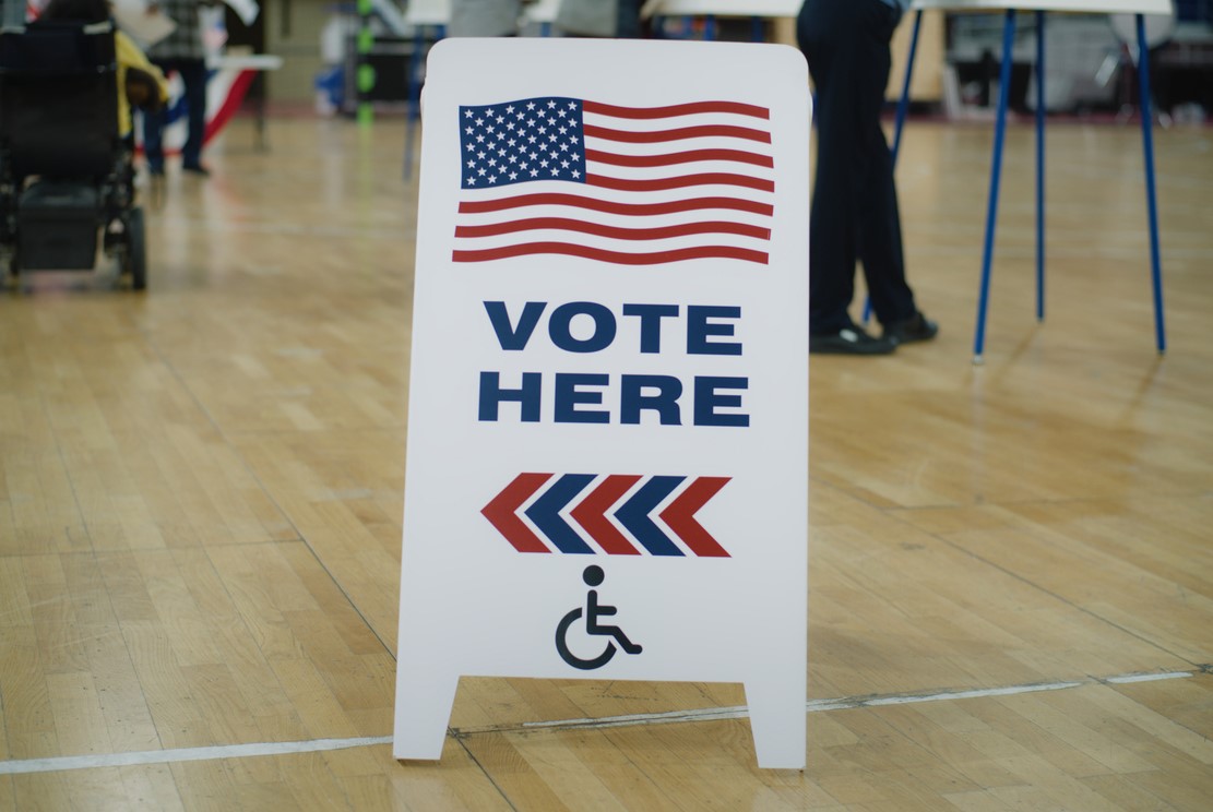 A vote here sign in a gymnasium that is serving as a polling place.