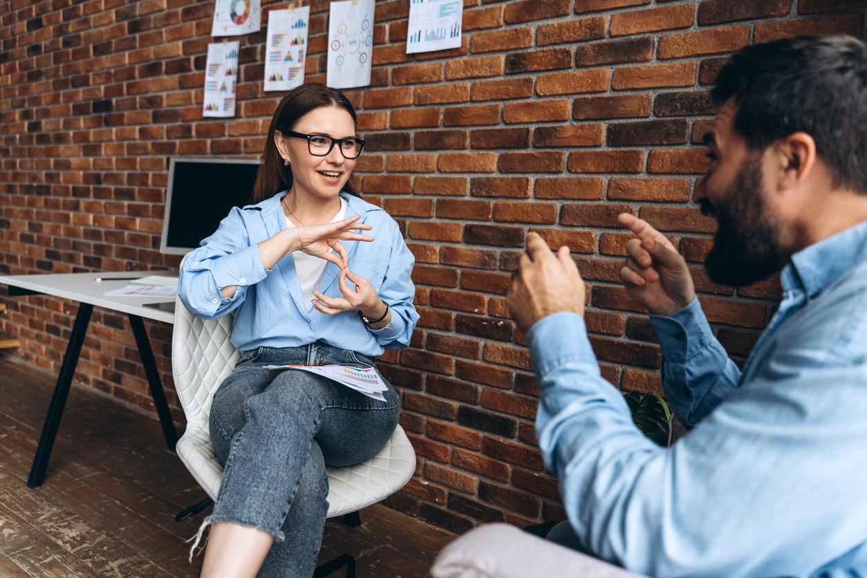 A man and a woman in an office communicating with sign language.