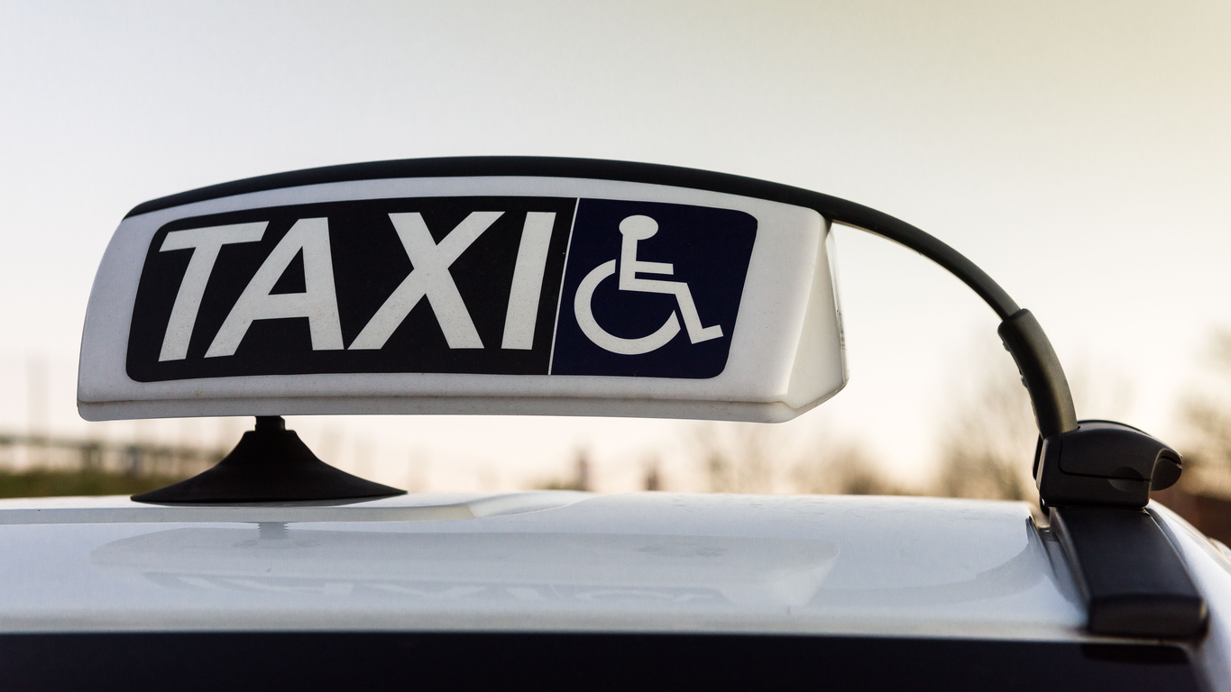 A sign on top of a car that says taxi and has an icon of a person in a wheelchair.