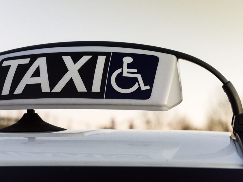 A sign on top of a car that says taxi and has an icon of a person in a wheelchair.